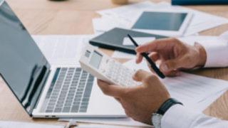 Main tenant un calculatrice devant un ordinateur portable sur un bureau