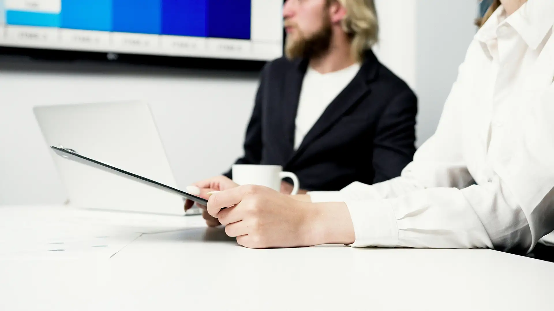 Les mains d'une femme qui tient une tablette et un collègue se tient à ses côtés lors de la réunion