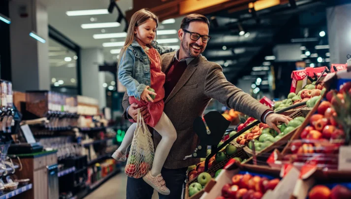 Un père tenant sa fille dans ses bras tout en faisant son épicerie