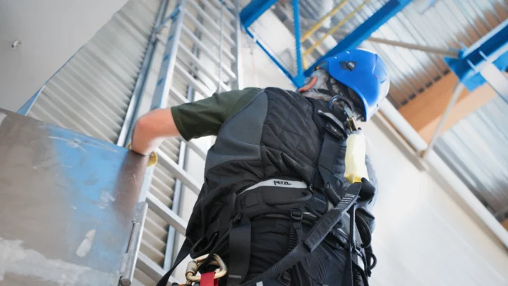 Homme doté d'un casque et d'un harnais montant une très haute échelle dans une éolienne