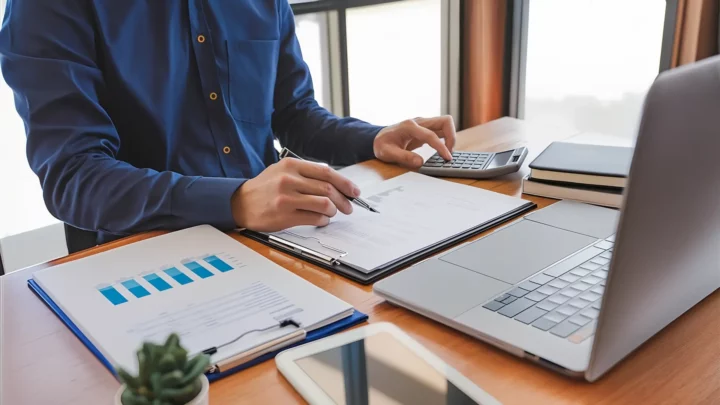 Professionnel analysant des données financières à l'aide d'un ordinateur portable, de rapports et d'une calculatrice